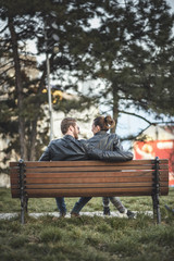 Young sweet couple embraced on a bench in park watching a beautiful sunset, enjoying their love and nature