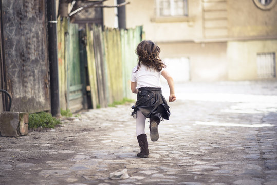Little girl running down a cobblestone alley