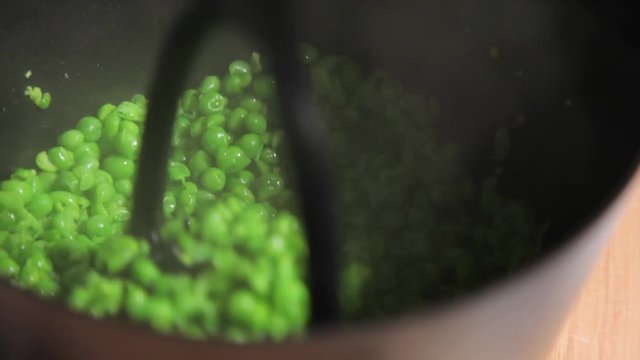 A close up shot of a woman smashing green pease in a pot.