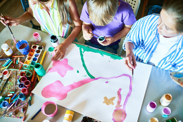 High angle view at  three children painting pictures with watercolors working together in art...