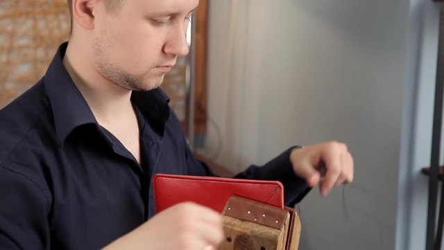 In the workshop, a man is sewing leather workpieces, making a wallet