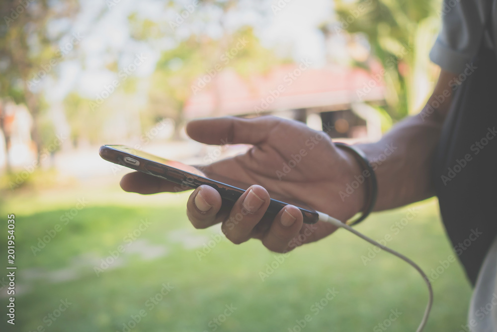 Poster hand of man using smartphone in park, he is typing messages with has friends through the chat applic