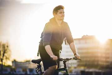 Young man riding a bicycle on the street, enjoying his activity in a sunset lit urban area