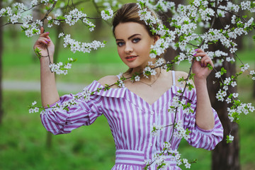 Beautiful blonde girl with blond hair in a dress on a background of spring blooming trees