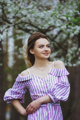 Fototapeta premium Beautiful blonde girl with blond hair in a dress on a background of spring blooming trees