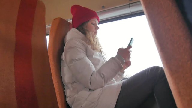 young cheerful woman in a red hat, traveling by bus on a sad day. She takes pictures on a smartphone