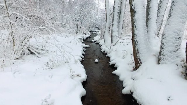 Small creek in winter snowy forest among snow banks