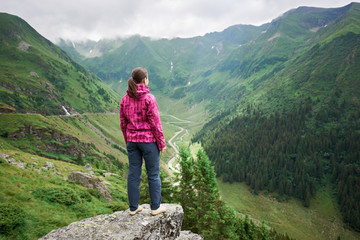 Female tourist enjoys the beautiful scenery of the valley of green mountains, clouds hanging over...