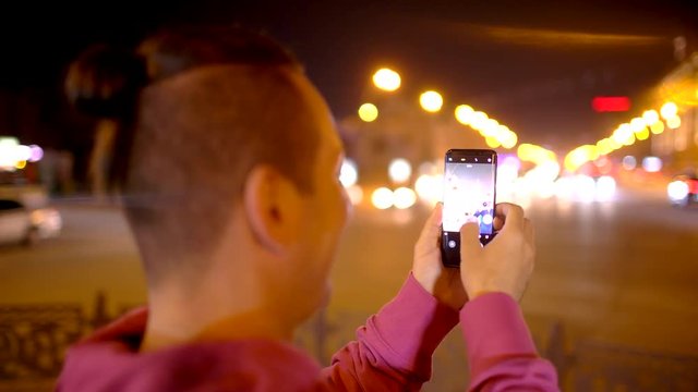 Man taking photo with camera phone at night city. Young casual man taking picture with camera phone outside. 4 k Young man with smartphone in night city. Technologies concept.