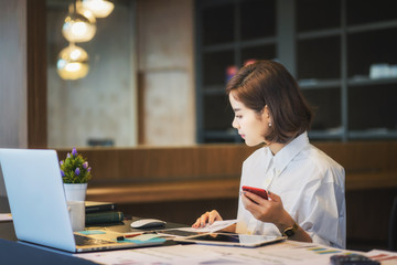 Beautiful woman using smartphone while working with laptop at modern office	