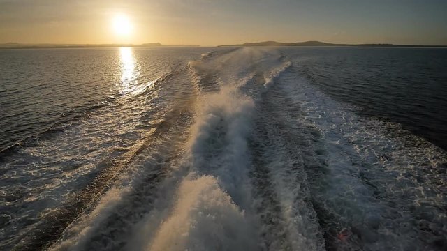 Background of water trail foaming behind a ferry boat. Sunset and evening time.