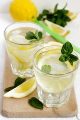 Lemonade with lemon slices, mint and ice and lemons on a light concrete background. Rustic style.