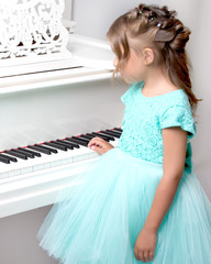 Beautiful little girl is playing on a white grand piano.