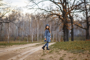 Obraz premium A cute girl in gey coat and gray hat in the oak wood in autumn walking at the sunset