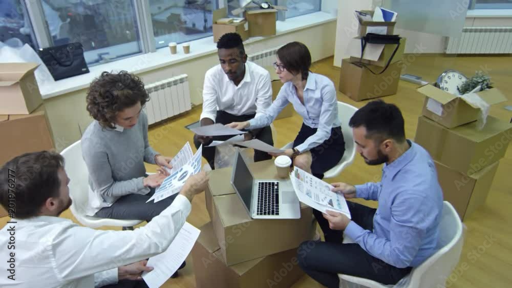 Poster high angle view of multiethnic business team sitting around stack of boxes after moving in new offic