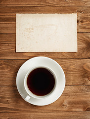 Fototapeta na wymiar cup of coffee on wooden boards, blank paper sheet with place for text - holiday and greeting concept