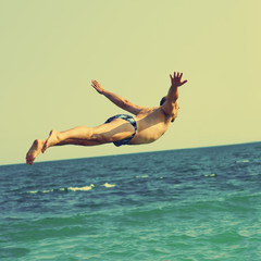 Sporty healthy man jumping into the sea during summer vacation, image with toning square aspect...