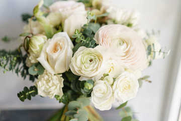 Fototapeta na wymiar Wedding bouquet of white roses and buttercup on a wooden table. Lots of greenery, modern asymmetrical disheveled bridal bunch