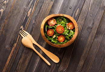 Salad with arugula, tomatoes and pine nuts in a wooden bowl,  top view