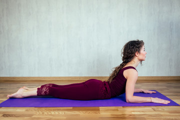 Fototapeta na wymiar happy beautiful woman with curly hair practicing yoga on a yoga mat on a gray wall background. concept of health practice, yoga and stretching