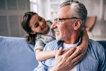 The happy girl hugs a grandfather on the sofa