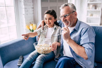 The little girl and a grandfather wathing television with a popñorn