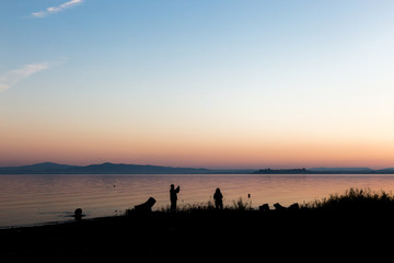 Silhouettes of a couple on a lake shore, taking photos of sunset