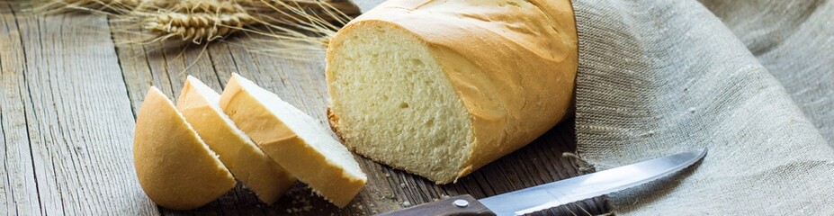 Banner of Sliced bread with wheat spikes on wooden table closeup