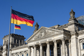 Obraz premium Niemcy, Berlin: Dwie flagi narodowe i słynna część głównego portalu wejściowego budynku parlamentu Deutscher Bundestag (dawny Reichstag) w centrum niemieckiej stolicy z błękitnym niebem.