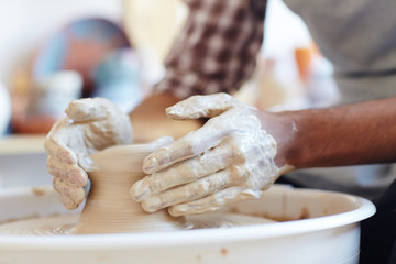 Close-up view of unrecognizable ceramic master making earthenware on pottery wheel in workshop