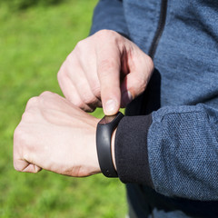 Fitness bracelet or smart watch on a man's hand. Against the background of green grass. An adult male in a blue band. Healthy lifestyle concept