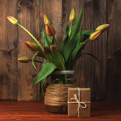 tulips in a decorative vase, on a wooden background. A gift in kraft paper. Vintage style congratulations, surprise.
