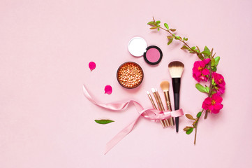 Various brushes for make-up and pink spring flowers on a pink pastel background top view with copy space. Makeup Accessories Top Flat Lay