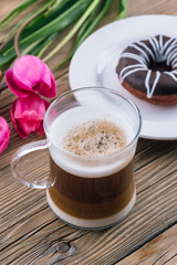 coffee with milk in a transparent mug, layers, mokyato, wooden table, tulips and donut, spring day