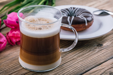 coffee with milk in a transparent mug, layers, mokyato, wooden table, tulips and donut, spring day