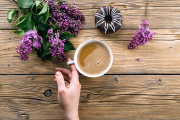 coffee in hand, a wooden table, a lilac and a donut, a spring day
