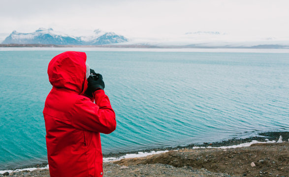 Nature travel photographer, person in red jacket taking photo of river in Iceland