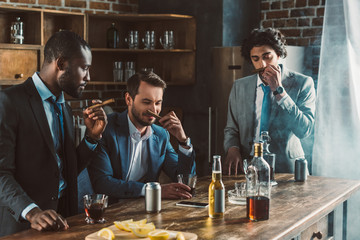 handsome young multiethnic men in suits holding cigars while partying together
