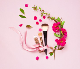 Obraz na płótnie Canvas Various brushes for make-up and pink spring flowers on a pink pastel background top view with copy space. Makeup Accessories Top Flat Lay