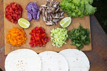 Mexican tacos ingredients. Set of sliced fresh vegetables with beef, lime and tortillas on wooden board. Top view. From above