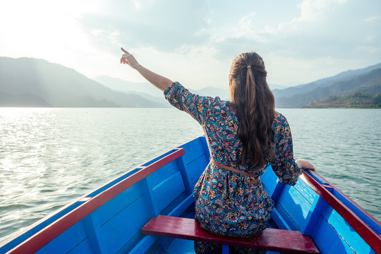 Young woman tourist in a beautiful dress is swimming on the lake by boat and enjoy the scenery of the mountains. the concept of outdoor activities. back view