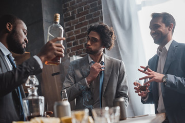 low angle view of young multiethnic businessmen smoking cigars and drinking whisky
