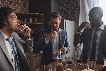 three young multiethnic friends in suits drinking tequila together