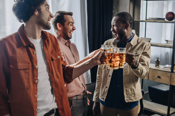 cheerful multiethnic male friends clinking beer glasses while partying together