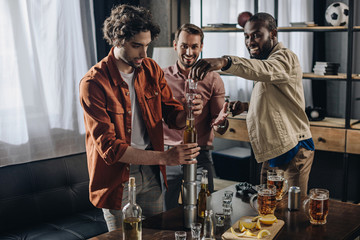 happy multiethnic male friends building tower from glasses and cans while partying together