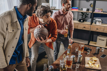 young multiethnic men playing with basketball ball and drinking beer together
