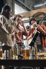 Fototapeta na wymiar happy young multiethnic friends drinking beer and playing guitar together
