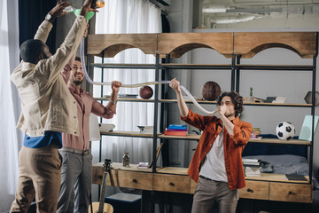 happy multiethnic male friends having fun and drinking from beer bong together