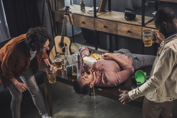 friends laughing and looking at man drinking from beer bong on table