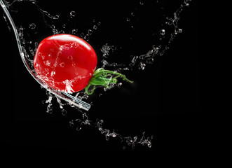 Red tomato on fork, water splashes